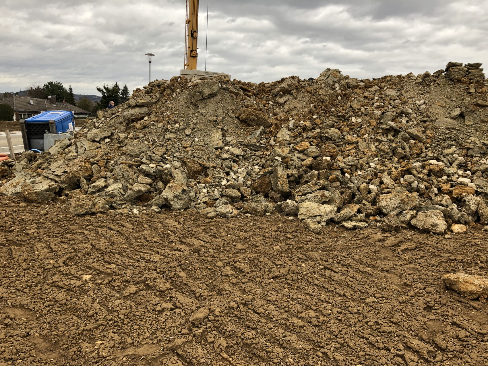 Grosser Stein- und Erdmuellhaufen auf Baustelle mit Bagger im Hintergrund