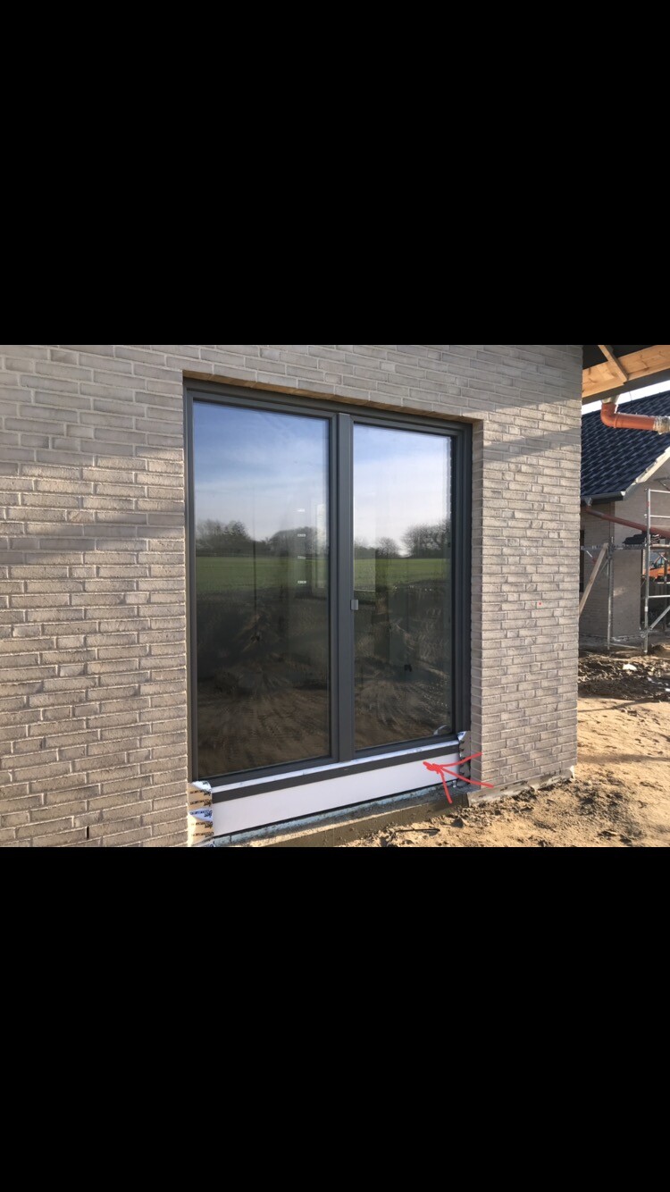 Große Glas-Schiebetür in einer Neubau-Backsteinwand; Baugelände mit Erde außen.