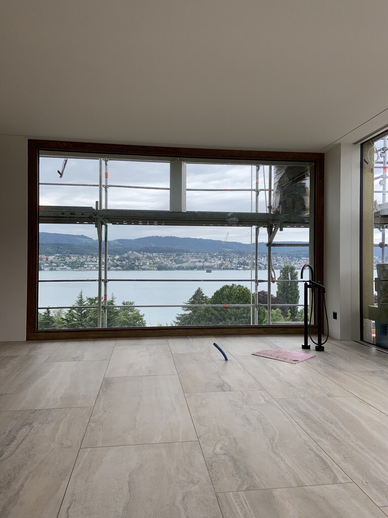 Innenraum mit großer Fensterfront, Aussicht auf See und Berge; Gerüst außen, Werkzeuge auf Boden