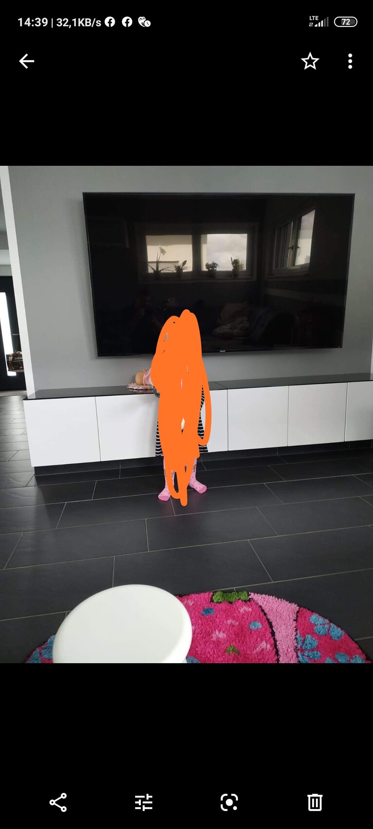 Großes Flachbildfernseher im Wohnzimmer vor weißem Lowboard und dunklen Bodenfliesen