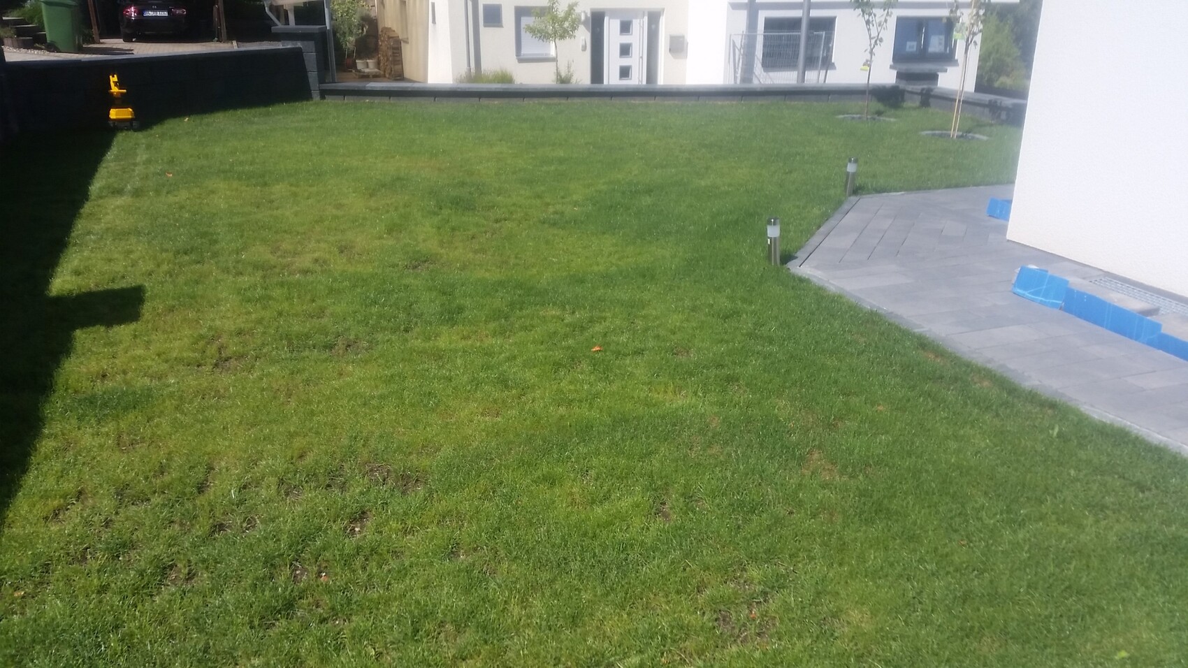 Grüner Rasen im Gartenbereich vor modernem Haus mit gepflasterter Terrasse und Leuchtpfosten