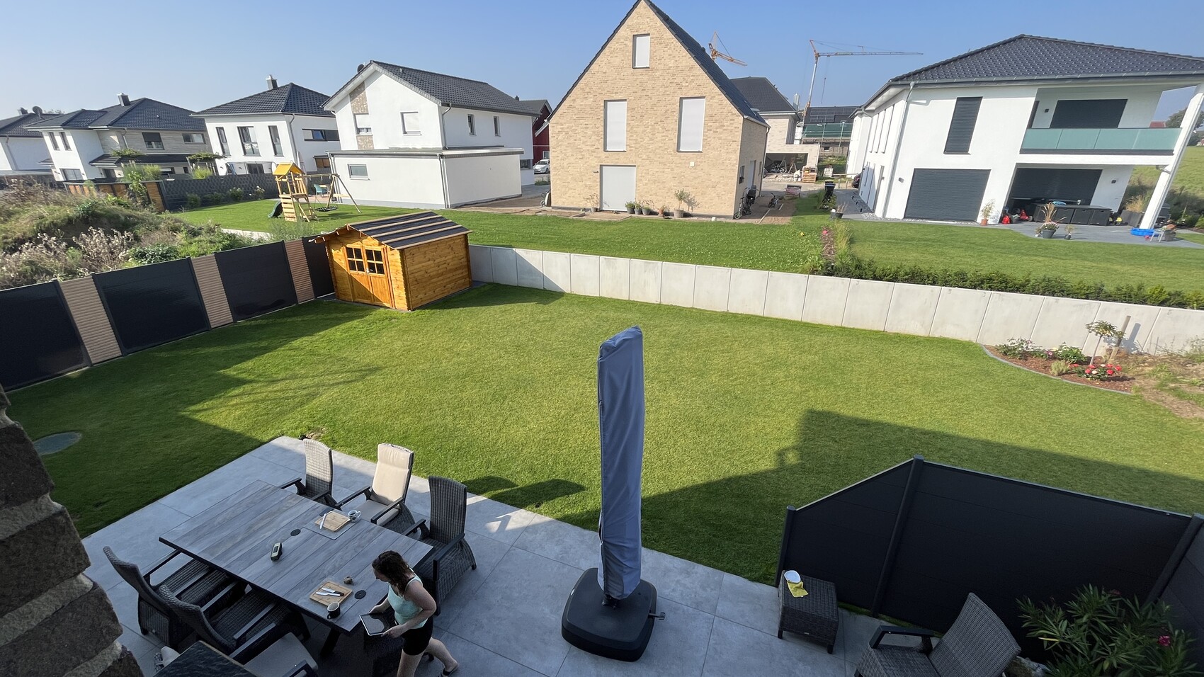 Hinterhof mit grünem Rasen, Holzgartenhaus, Spielgerät und Esstisch auf Terrasse.