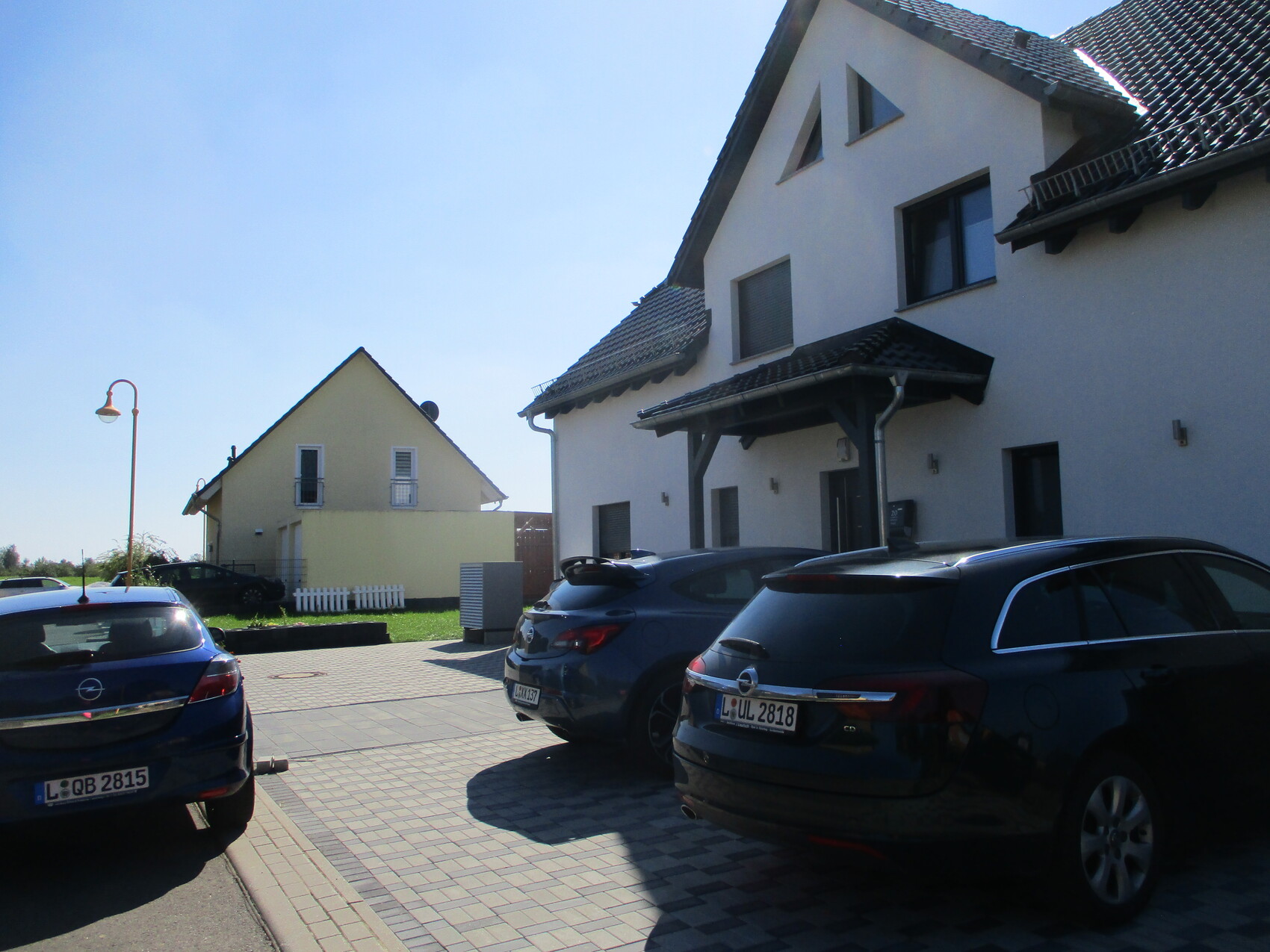 Großes weißes Haus mit dunklem Dach; daneben gelbes Haus, geparkte Autos.