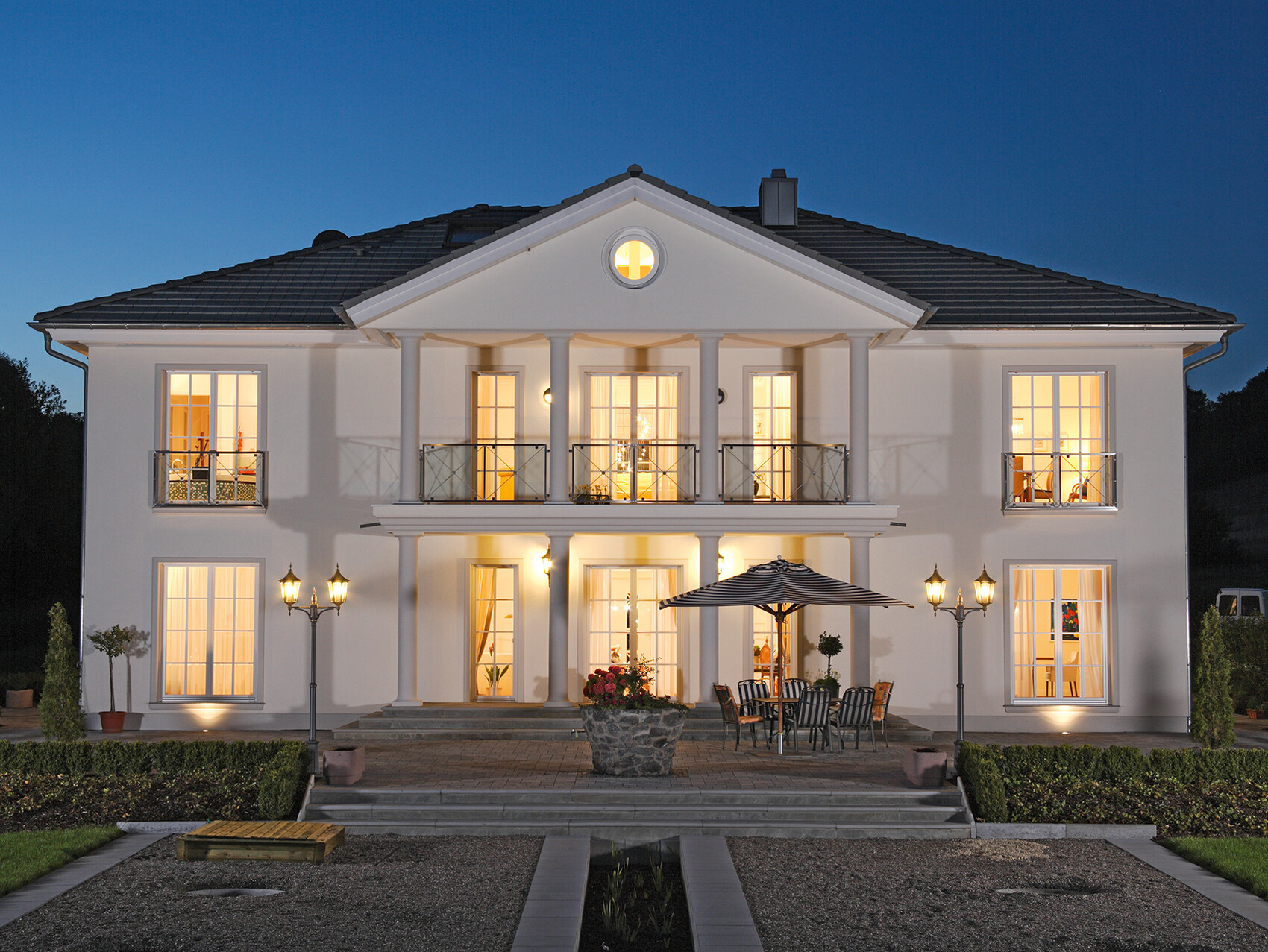 Weiße zweistöckige Villa mit Säulen-Portal, Balkon und Terrasse im Abendlicht.