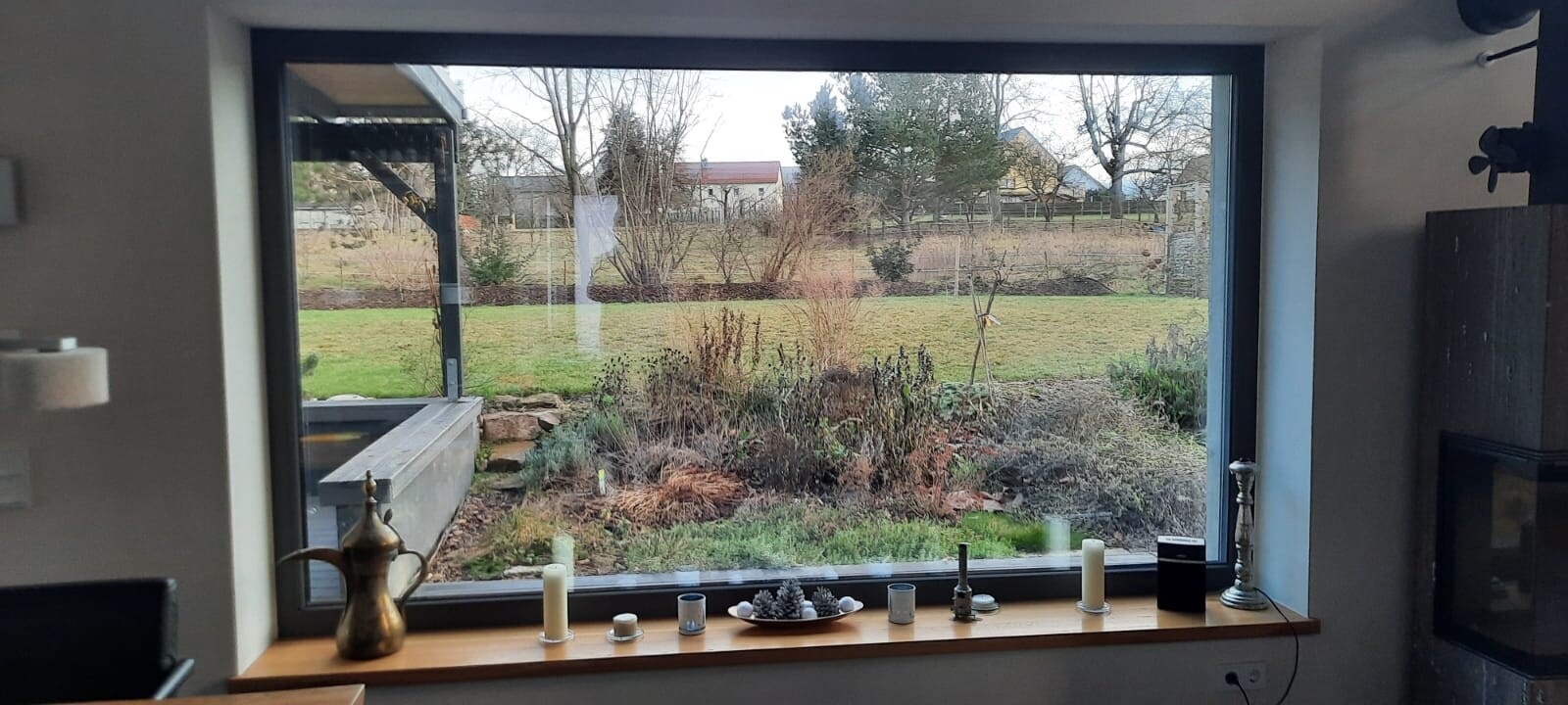 Blick durch großes Fenster auf Gartenszene; Teekanne, Kerzen und Deko auf Fensterbank.