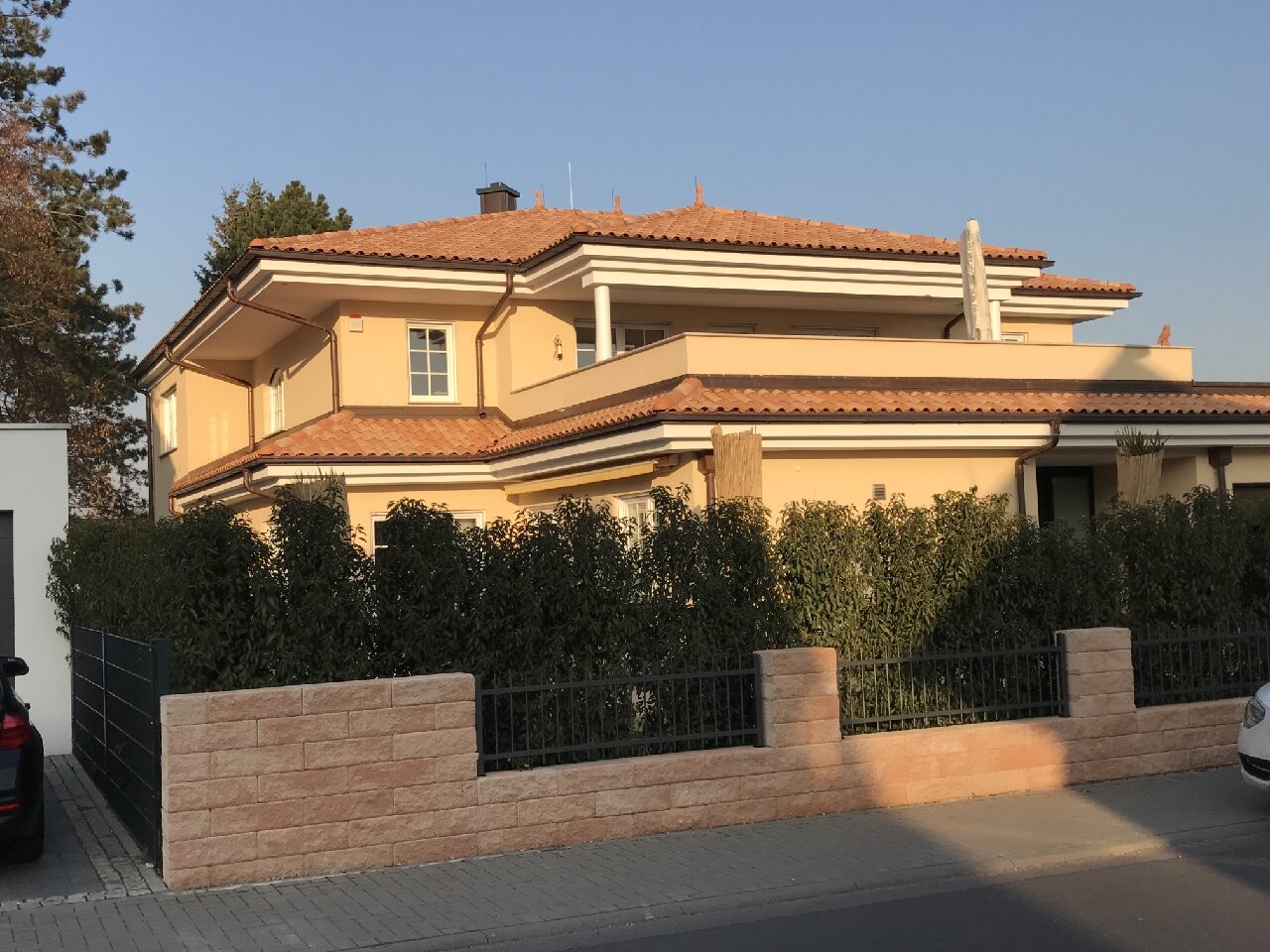 Großes zweistöckiges Haus mit oranger Fassade, rotem Ziegeldach, Balkon und Hecke.