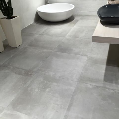 Modernes Badezimmer mit einer freistehenden weißen Badewanne, grauen Fliesen und schwarzem Waschbecken.