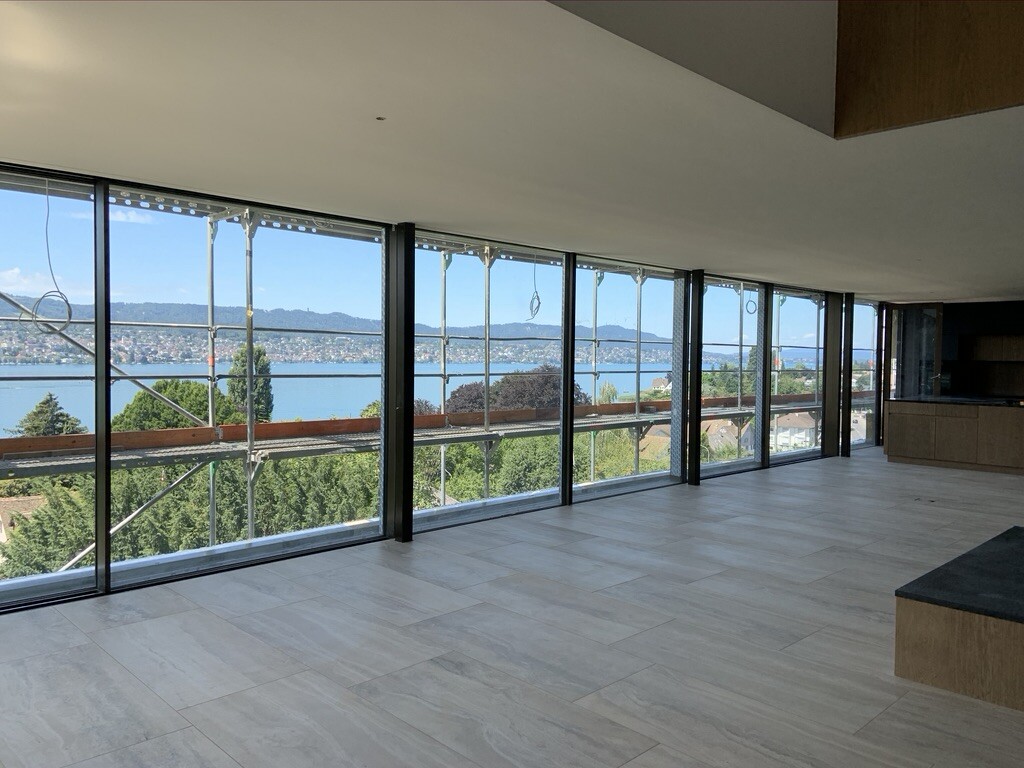 Leeres modernes Wohnzimmer mit bodentiefen Fenstern, Baugerüst außen, Aussicht auf den See.