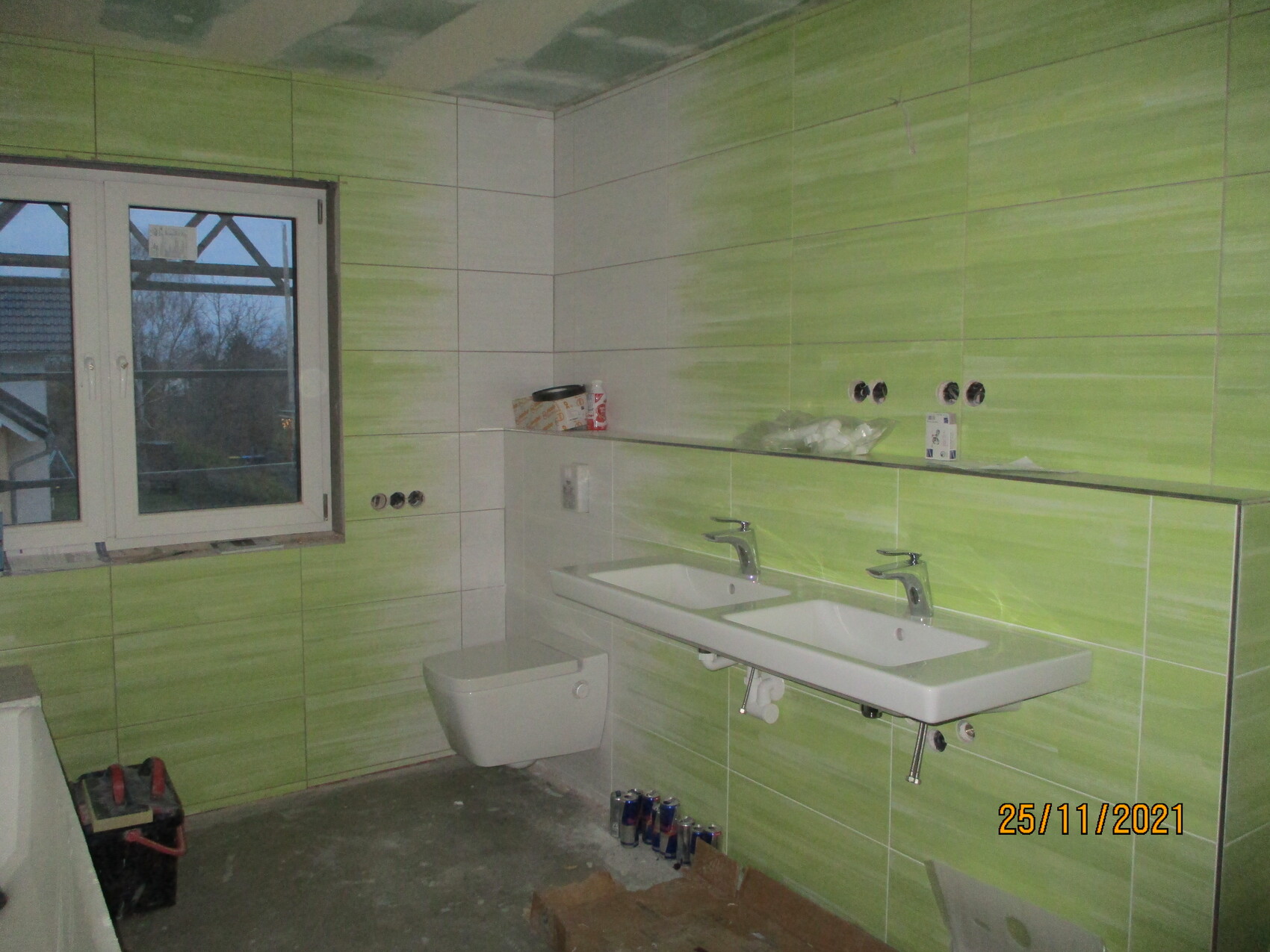 Badezimmer im Bau mit grünen Fliesen, Doppelwaschbecken, Toilette und Fenster.