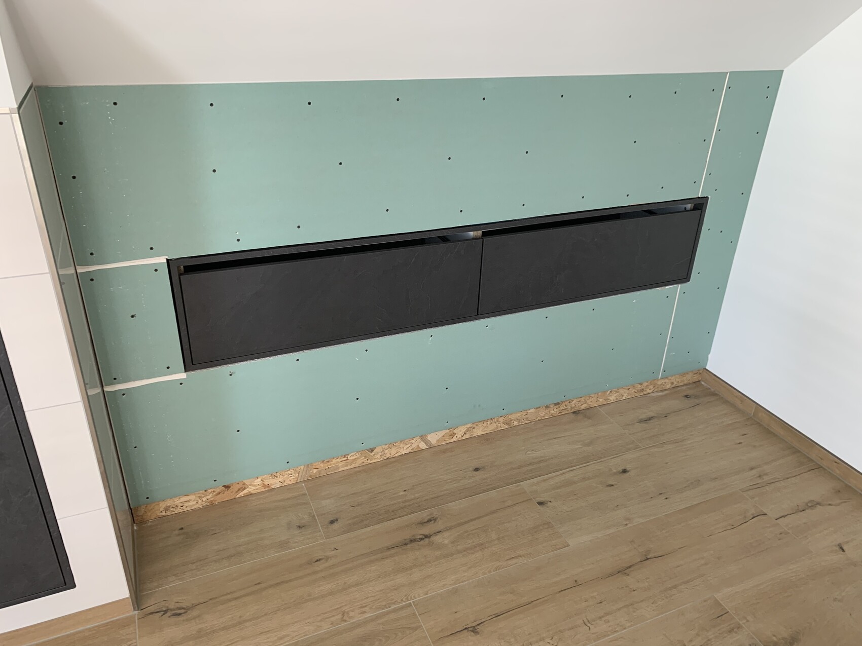 Halbfertige Wand aus grünem Trockenbau mit Schrauben; horizontale schwarze Schrankfront.