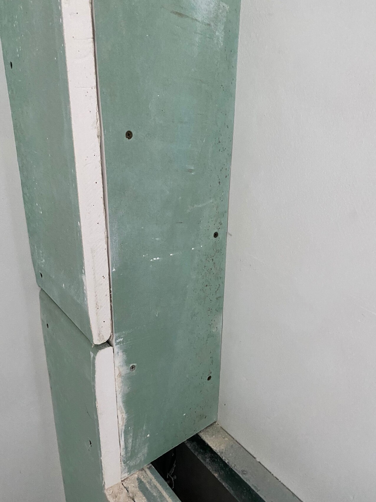 Nahaufnahme einer grün gestrichenen Türverkleidung mit weißem Rand, Schrauben sichtbar.