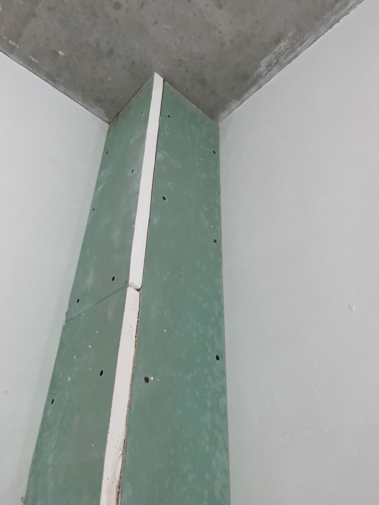 Grüne Trockenbauwand mit weißer Fuge und Schraubenlöchern, Beton-Decke sichtbar.