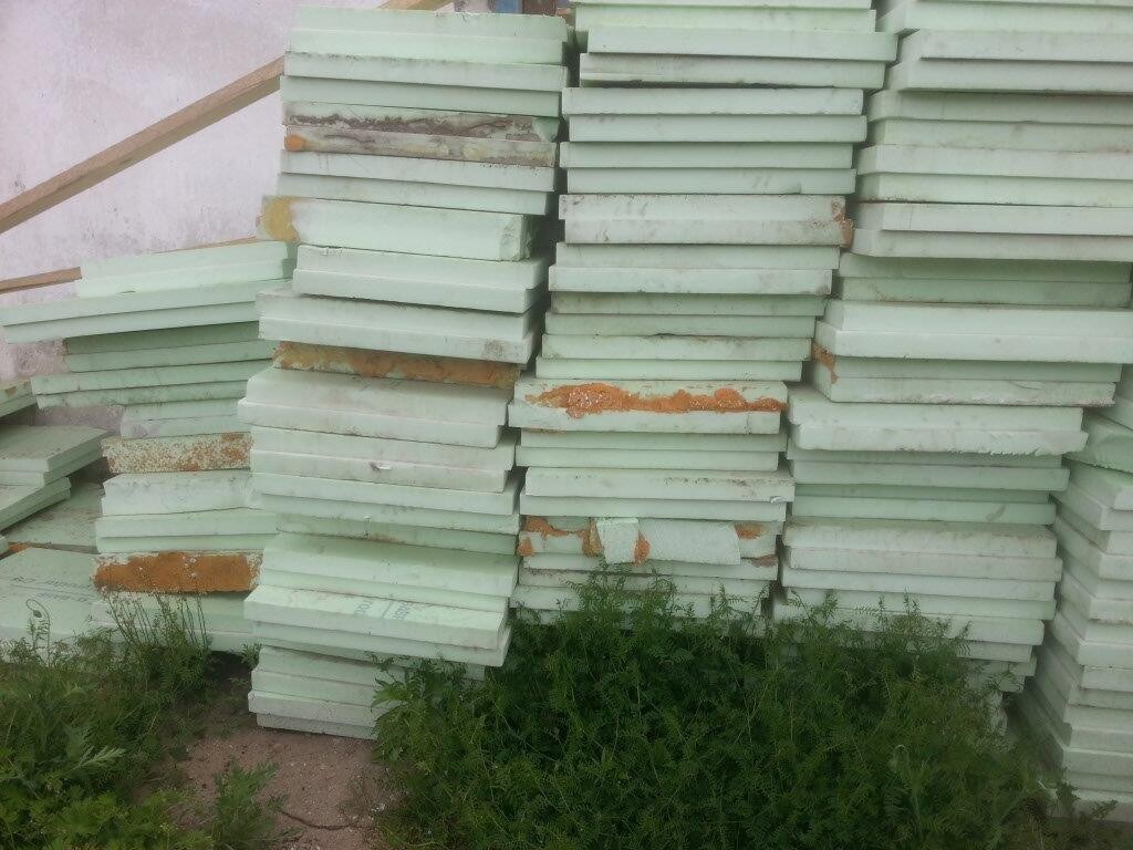 Mehrere grüne Dämmplattenstapel im Freien, Rostflecken, Gras davor.
