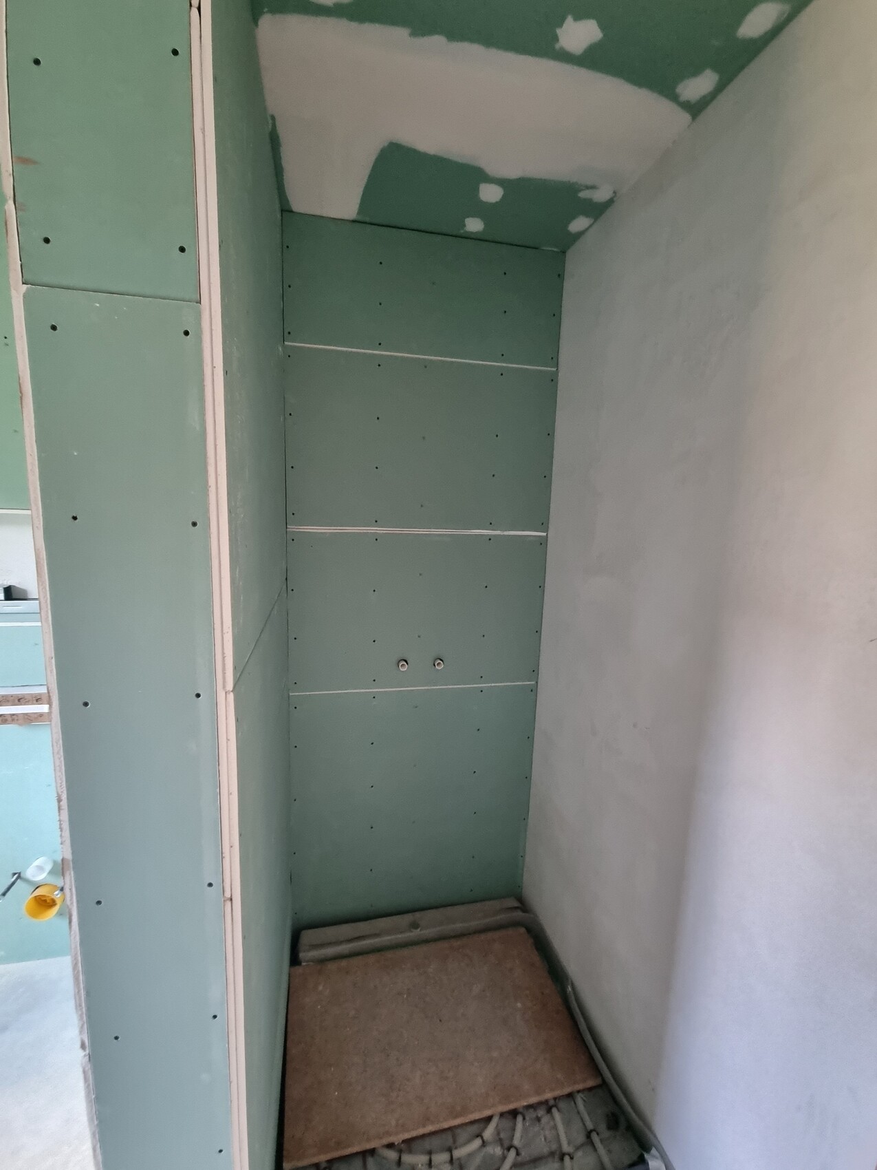 Rohbau-Nische mit grünen Gipskartonplatten an Wänden und Decke; Boden uneben.