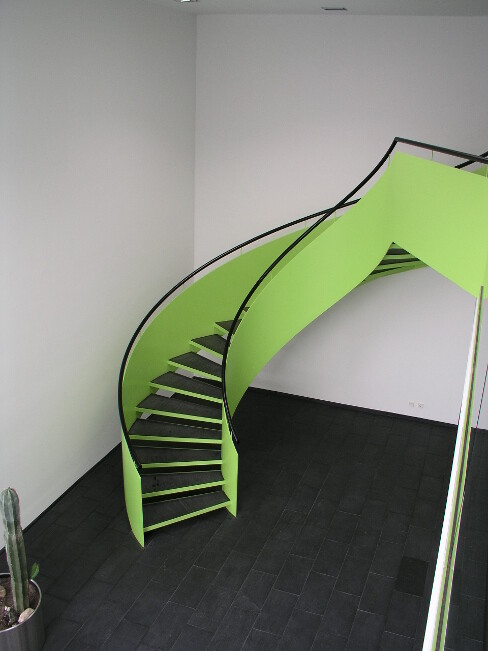 Grüne spiralförmige Treppe im Innenraum vor weißen Wänden und dunklem Boden.