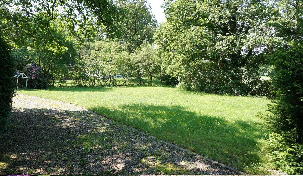 Grüner Garten mit Rasen, Bäumen, Kiesweg links und kleinem Pavillon im Hintergrund