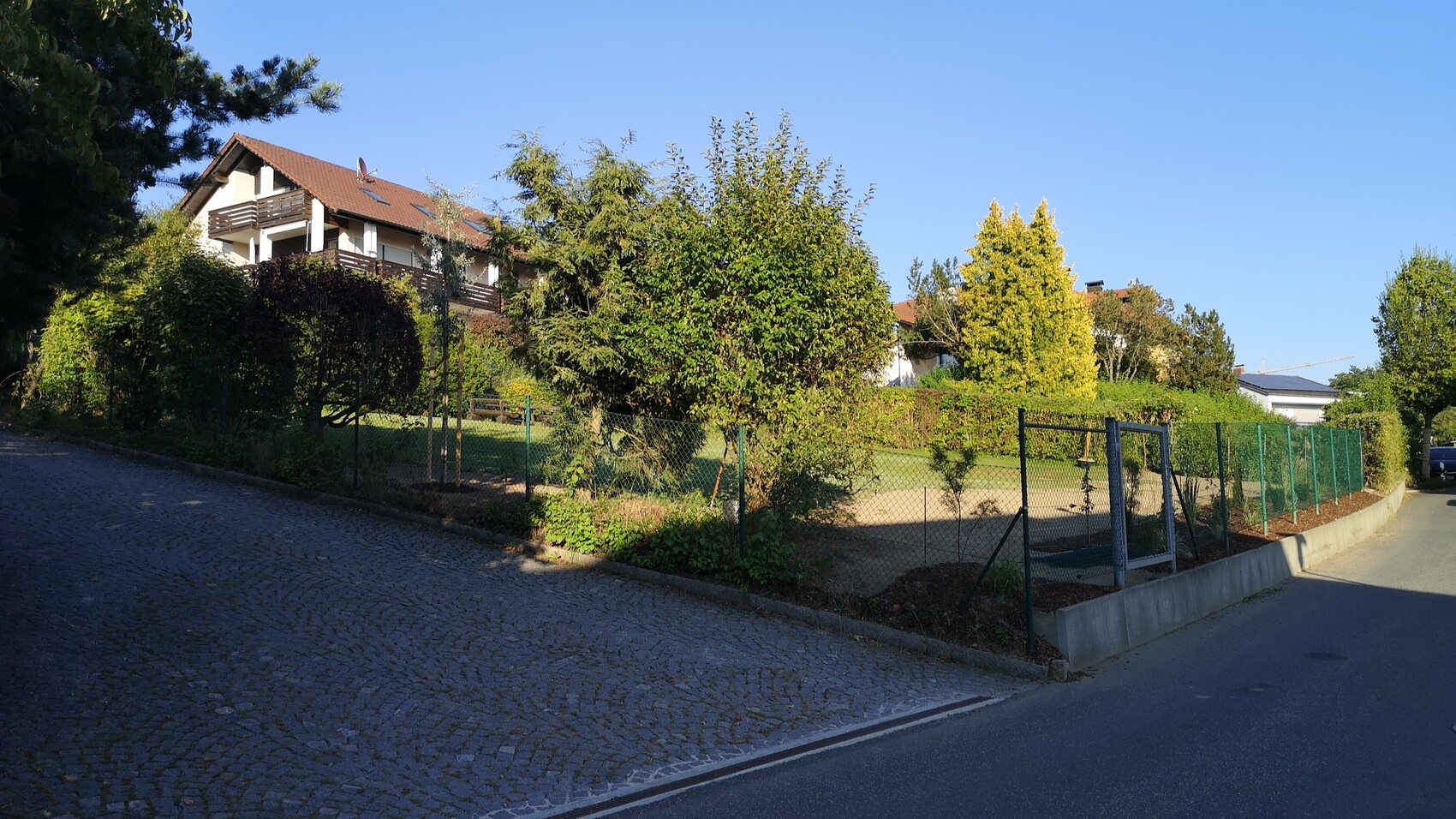 Straßenansicht eines Hauses mit Garten, Zaun und Bäumen