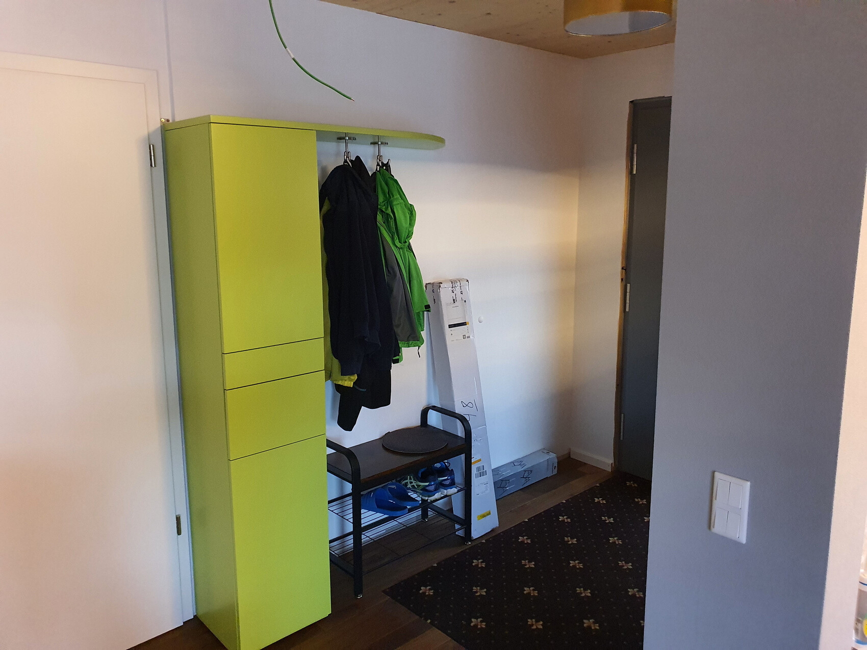 Heller grüner Flurschrank mit Jacken an der Garderobe, Schuhbank darunter und eine Leiter im Flur