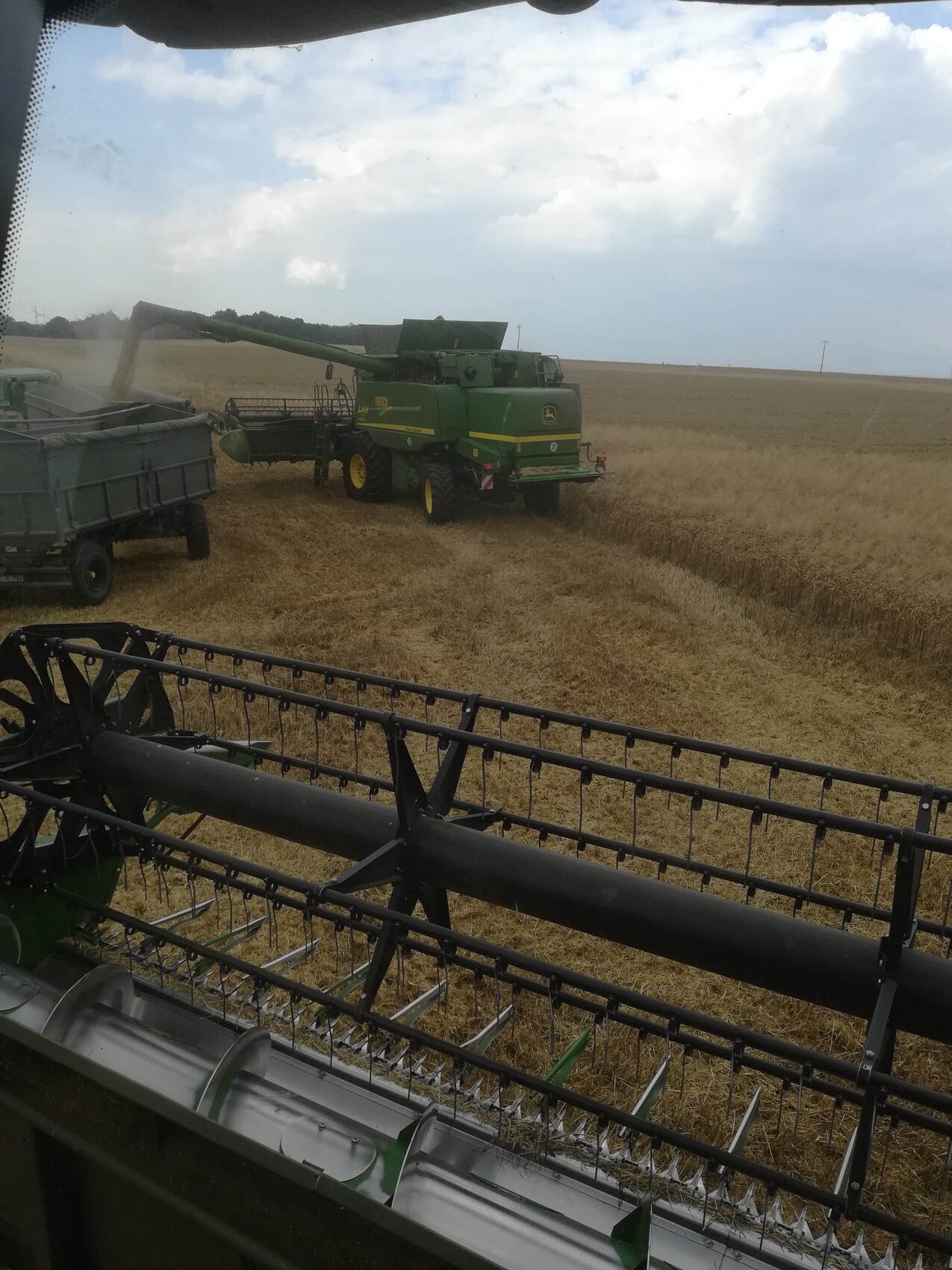 Grüner John-Deere Mähdrescher erntet Weizen; Blick aus Kabine auf eine weitere Erntemaschine.