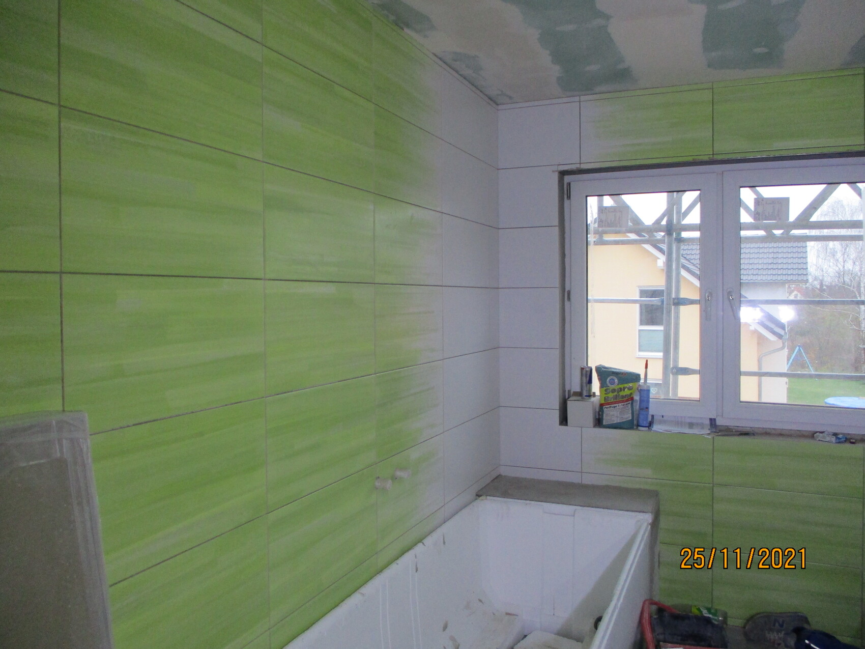 Badezimmer unter Renovierung: hellgrüne Wandfliesen, weiße Badewanne, Fenster mit Baugerüst.