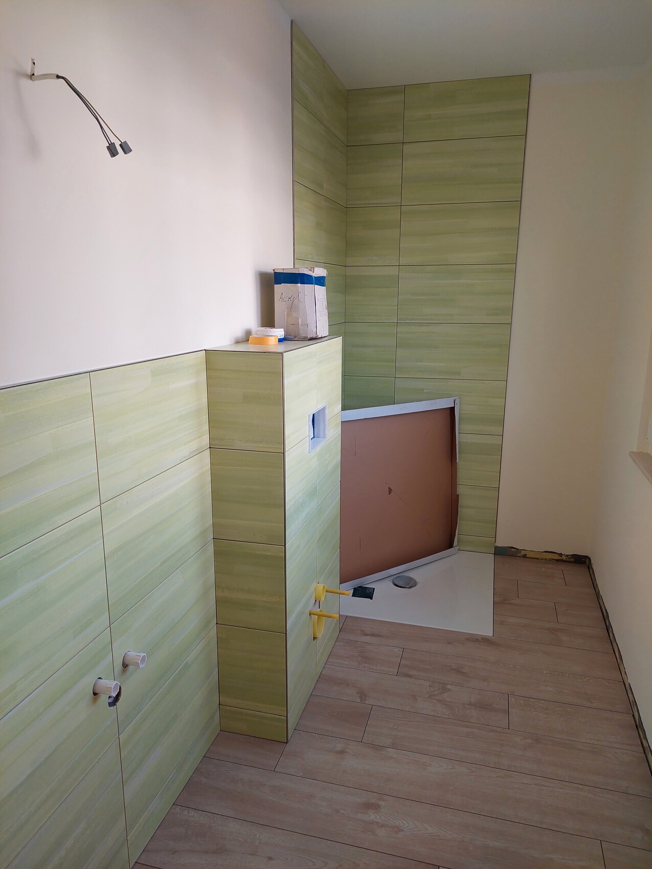 Teilweise fertig renoviertes Bad mit grünen Wand- und Bodenfliesen, unbelegter Duschbereich