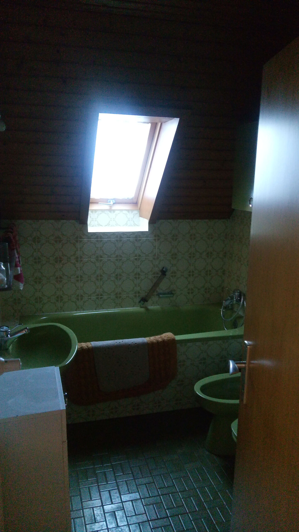 Grünes Badezimmer mit Badewanne, Waschbecken und Dachfenster unter Holzbalkendecke.