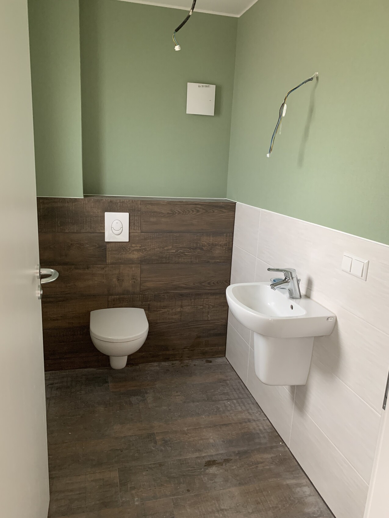 Badezimmer im Umbau: grüne Wände, Wand-WC, Waschbecken und freiliegende Kabel.