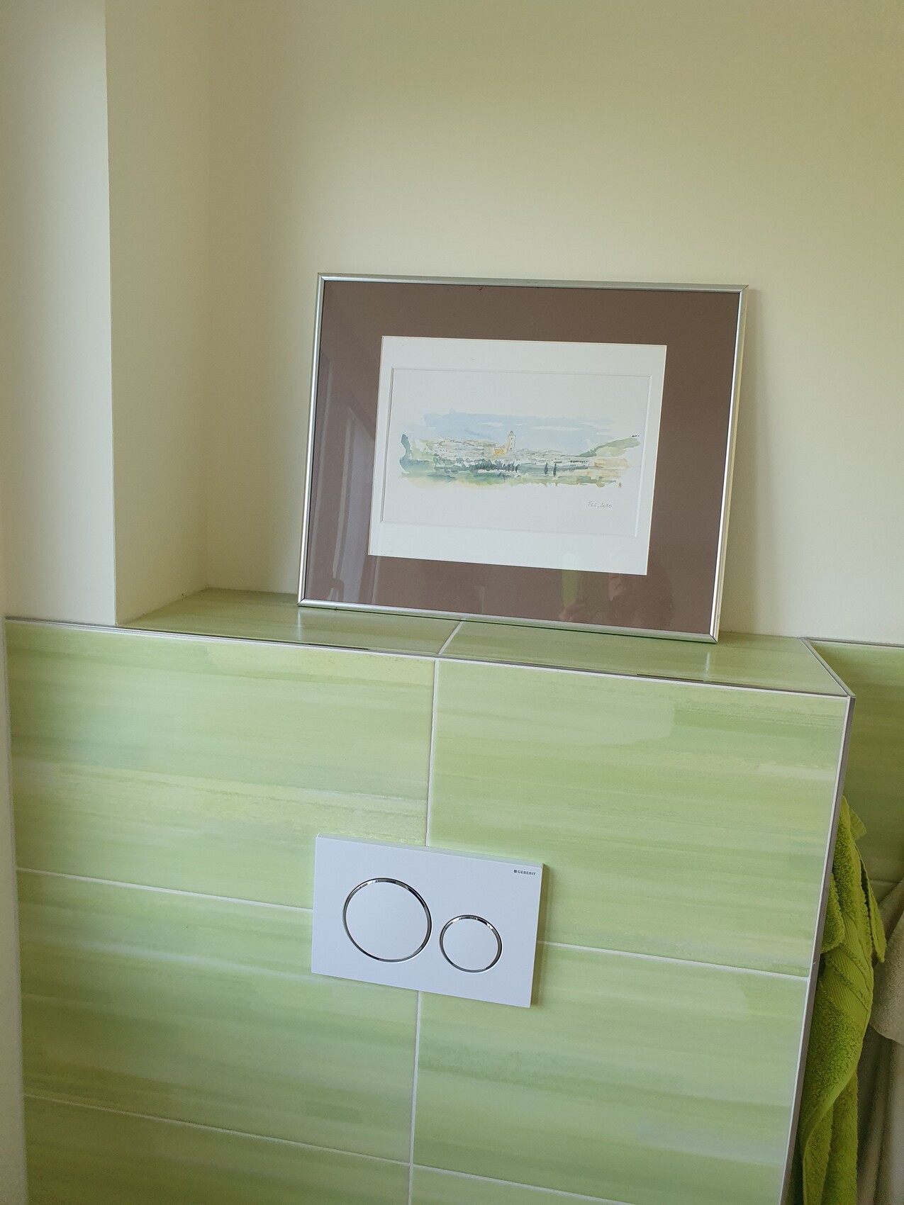 Aquarellbild in braunem Passepartout auf grün gefliester Wand; darunter WC-Spülplatte mit zwei Kreisen.