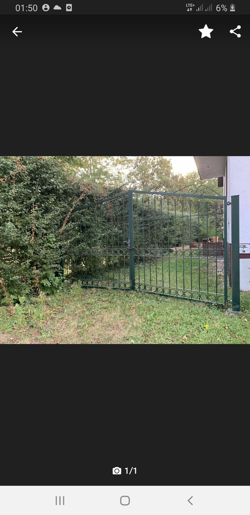 Grüner schmiedeeiserner Gartentor mit Zierleisten; Bäume, Gras und Gebäude im Hintergrund.