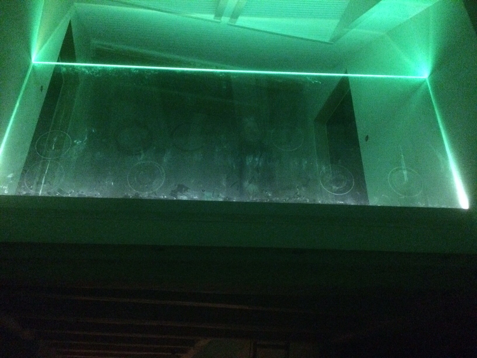 Grünes Licht in leerem Glasbehälter mit Neonrand; Boden mit Kreisformen markiert