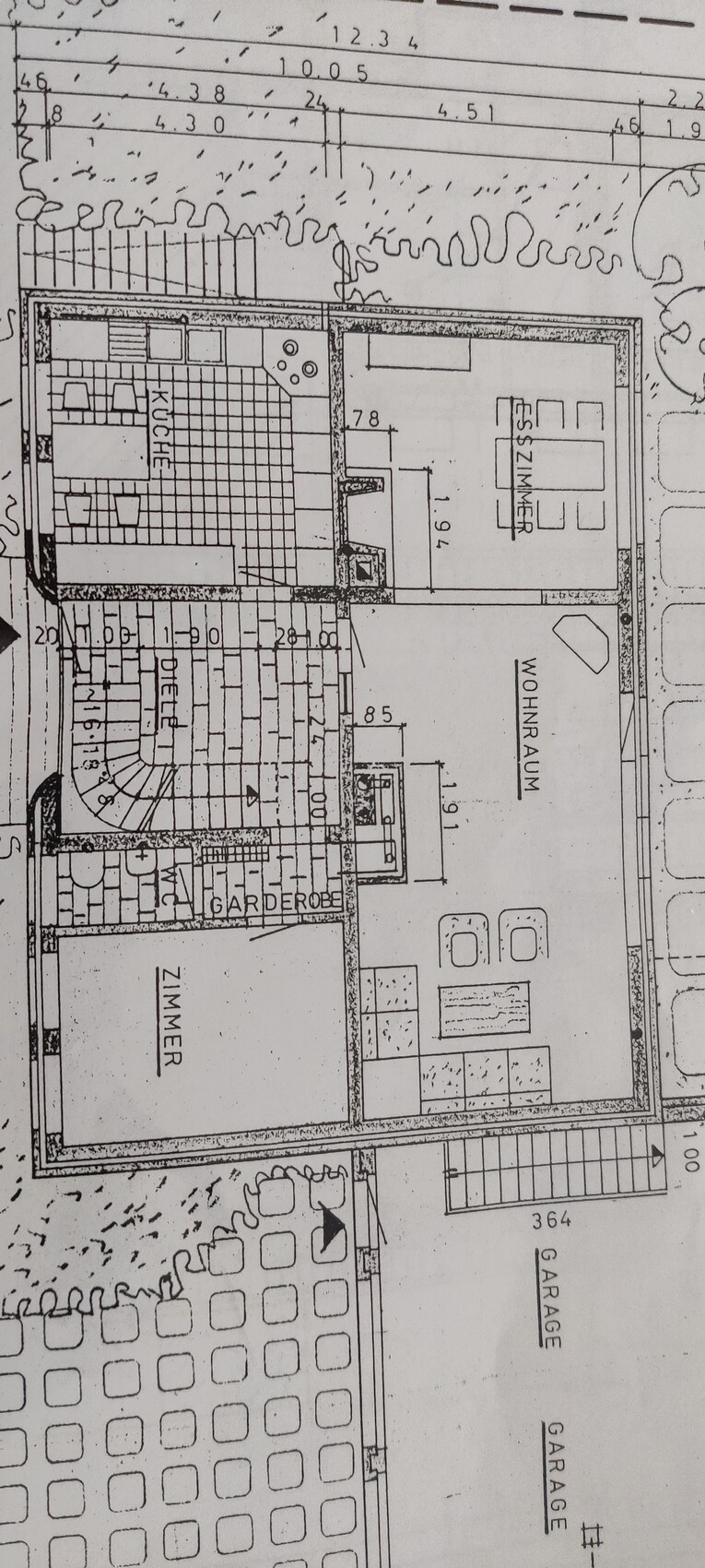 Grundriss eines Hauses mit Küche, Esszimmer, Wohnzimmer, Zimmer, Garderobe, Garage und Garten.