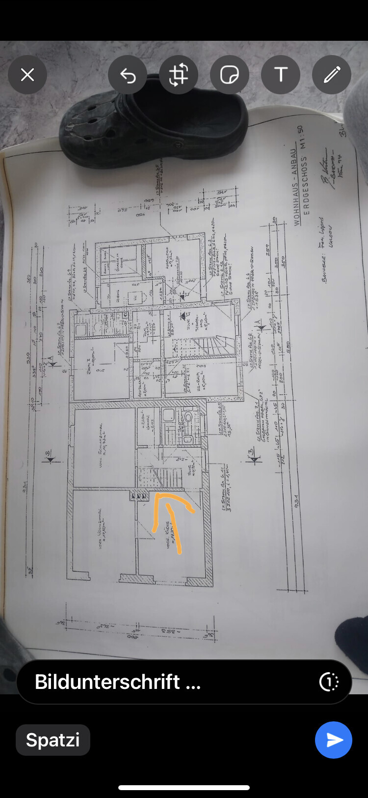 Grundriss eines Wohnhauses, schwarze Crocs-Sandale liegt auf dem Plan, orange markierter Raum.
