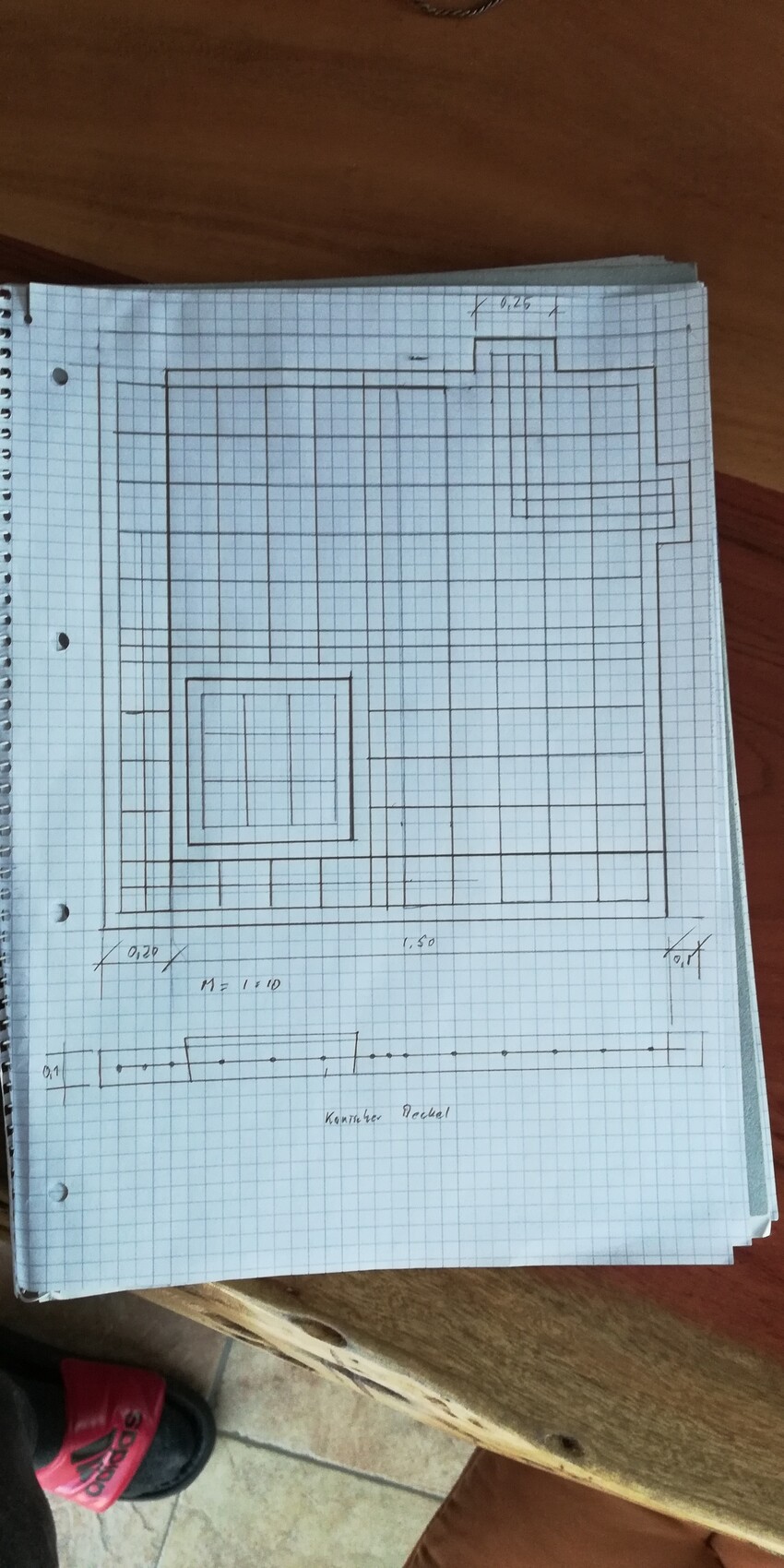 Auf kariertem Papier gezeichneter Gebäude-Grundriss mit Außenkontur, Innenräumen und Maßlinien.