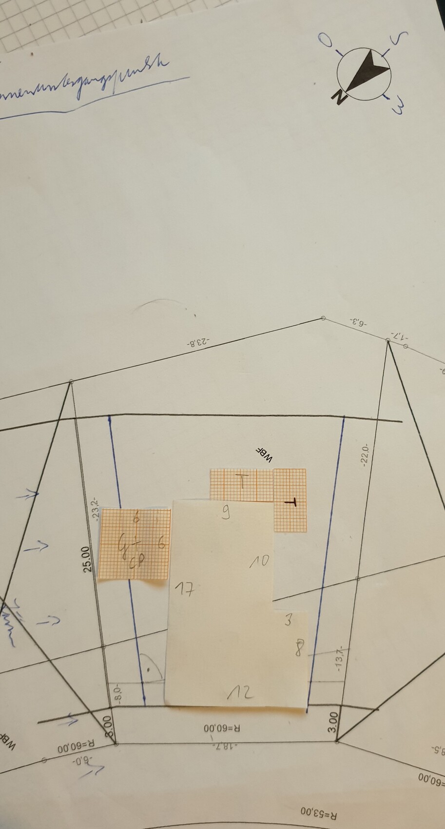 Grundriss eines Baugrundstücks mit Messlinien, Kompass und Klebezettel mit Zahlen.