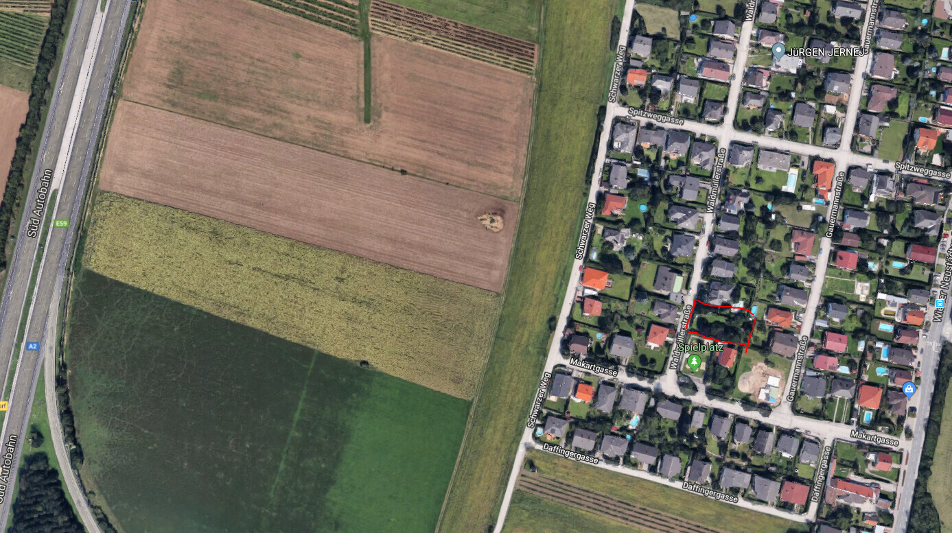 Luftbild: Felder links, Wohnviertel rechts; roter Umriss markiert ein Grundstück nahe Spielplatz.