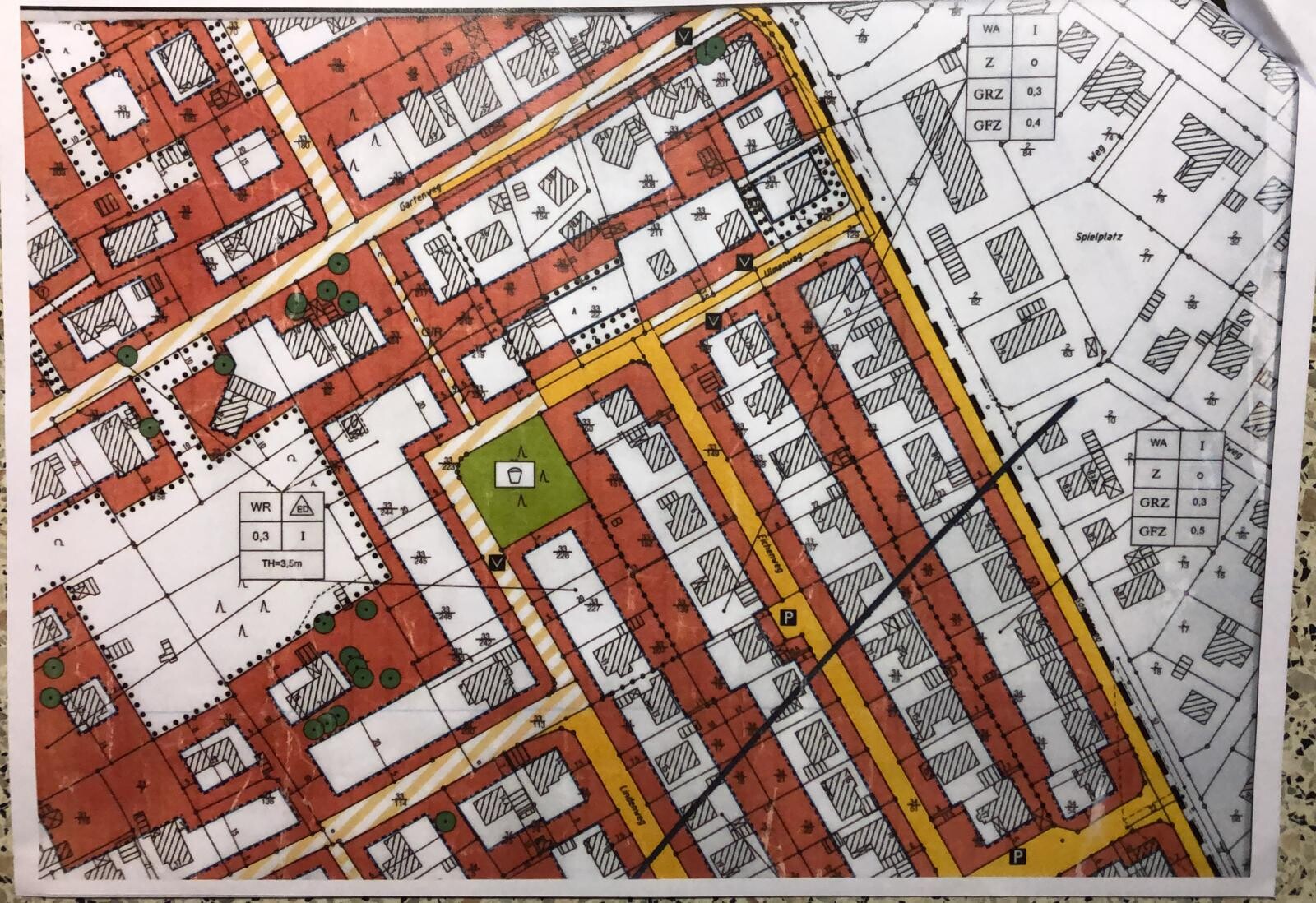 Stadtplan mit roten Bauzonen, gelben Straßen, grünem Parkbereich und Verkehrsachsen.