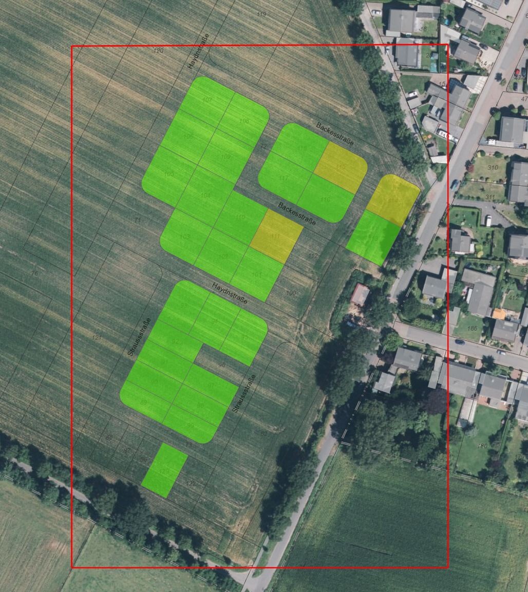 Luftbild eines Feldareals mit grünen und gelben Parzellen innerhalb eines roten Rahmens neben einer Siedlung.