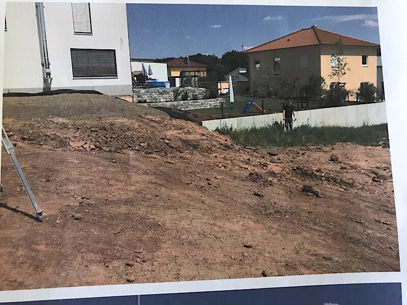 Baustelle mit Erdreich, Hang und angrenzenden Wohnhäusern, Bodenarbeiten sichtbar