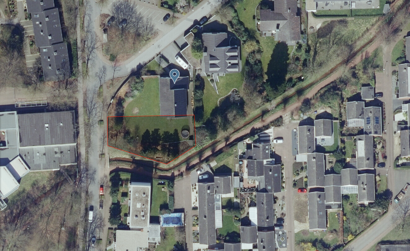 Luftaufnahme eines Wohngebiets; rotes Polygon markiert eine Grünfläche mit Bäumen neben einem Kanal.