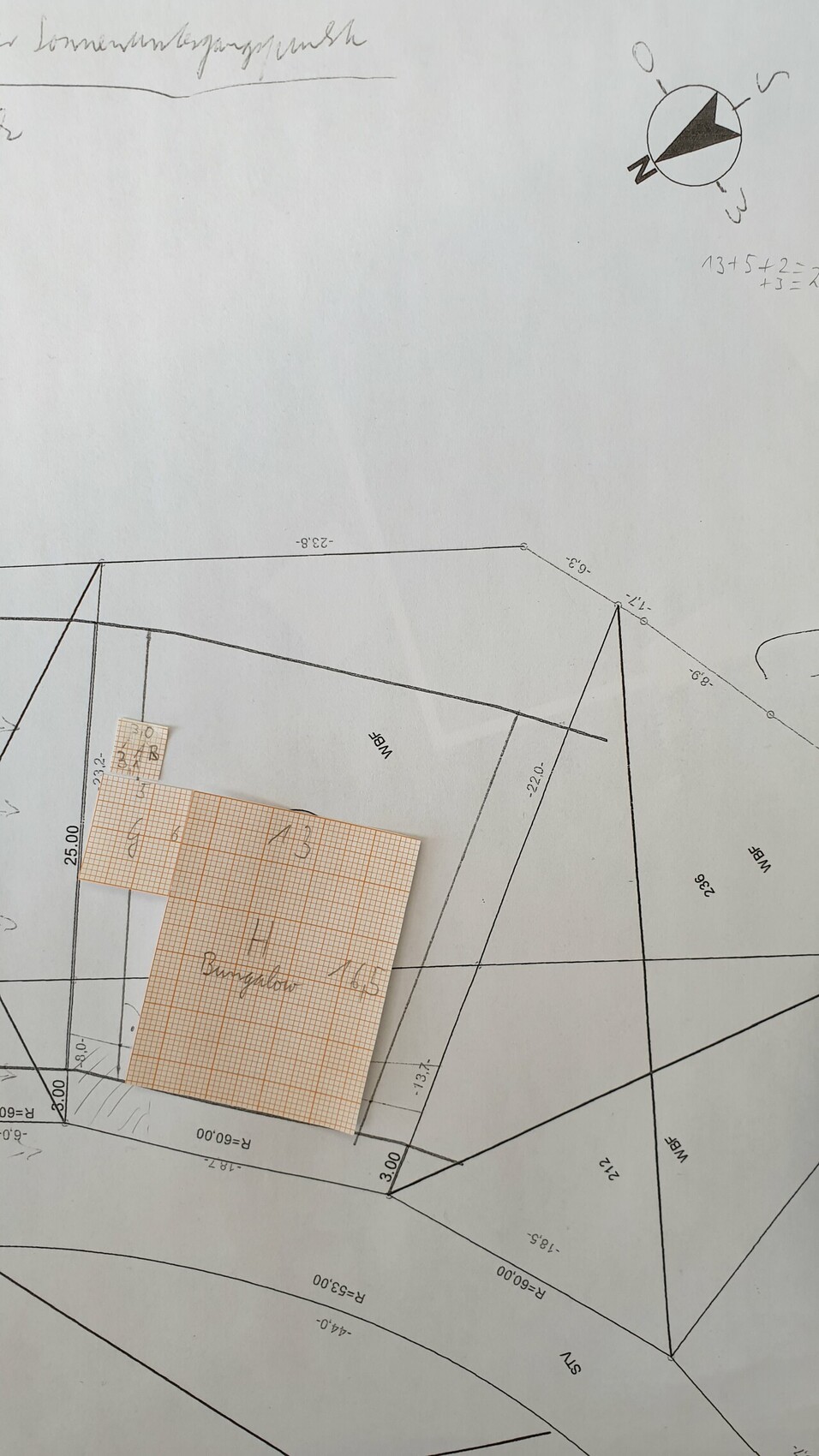 Grundstücksplan mit Linien, Maßen, Winkeln und Kompass; orange kariertes Blatt aufgeklebt