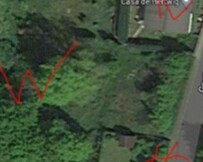 Luftaufnahme eines grünen Grundstücks mit roten Planmarkierungen am Weg.