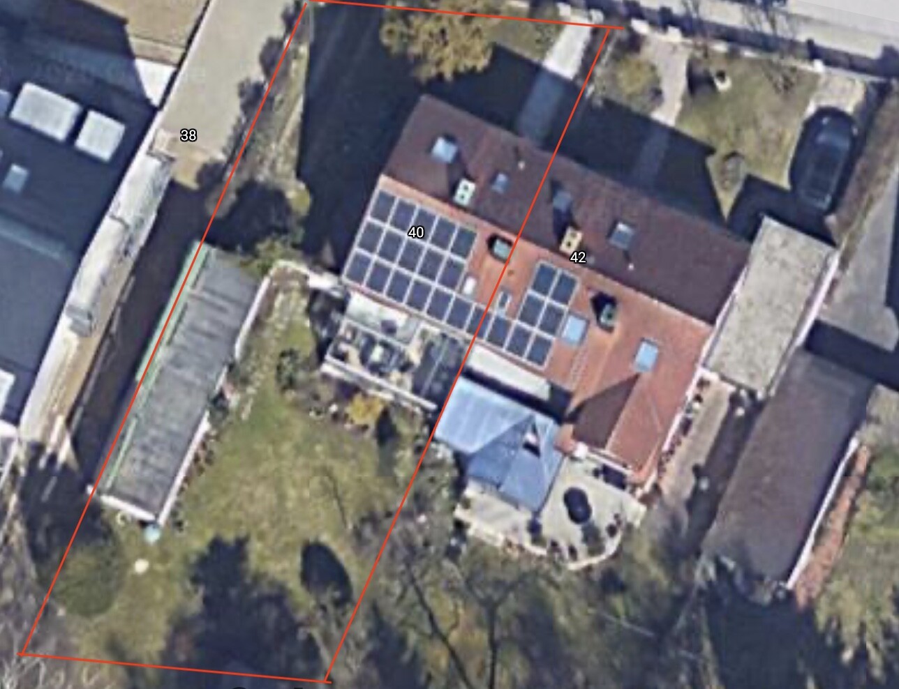 Luftbild eines Hauses mit rotem Ziegeldach, Solarmodulen und roter Grundstücksgrenze.