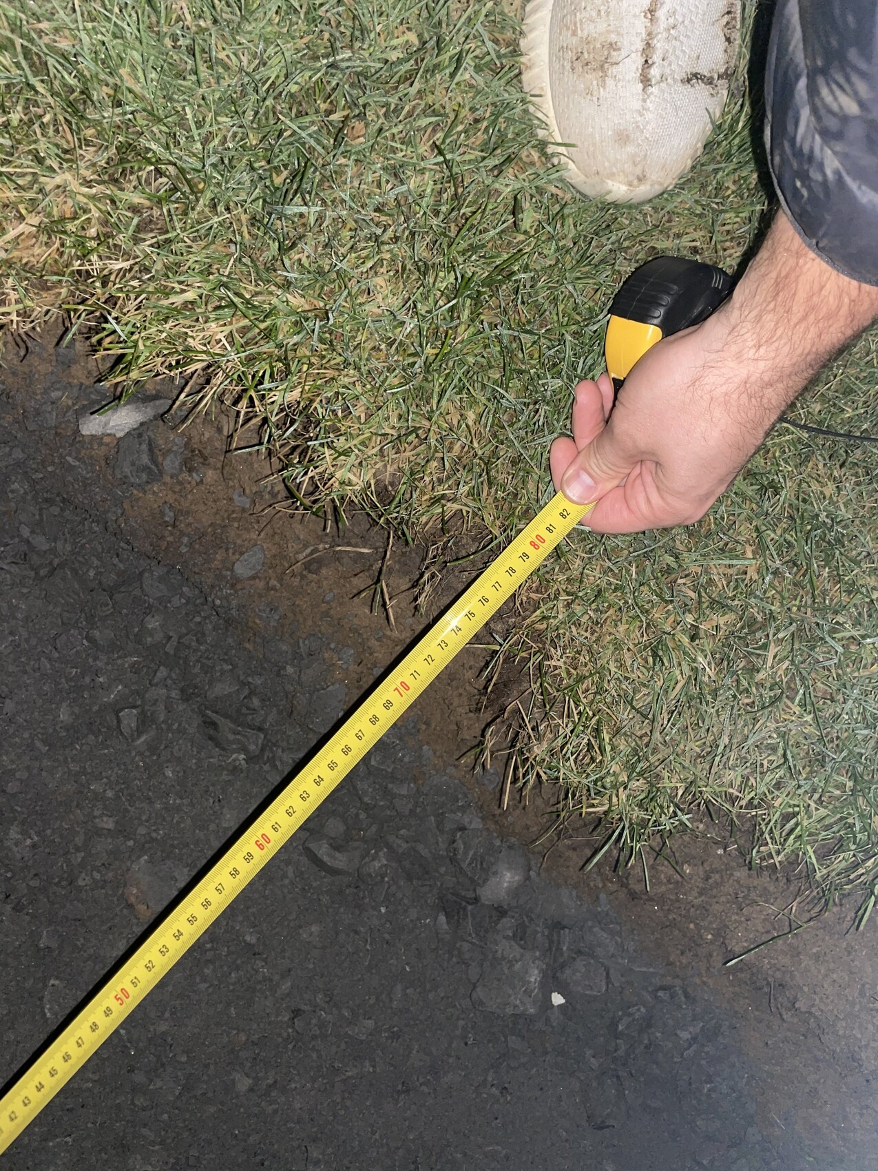 Person misst Baugrundstueck mit Tape-Maßband auf Gras und Erdoberflaeche.