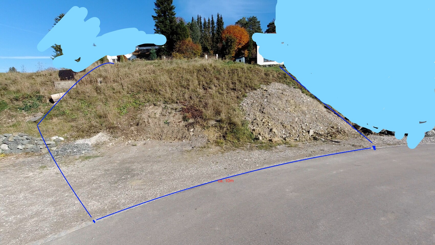 Steiler Kieshügel neben Straße, blaue Linien markieren Grundstücksgrenze; Hintergrund Bäume.