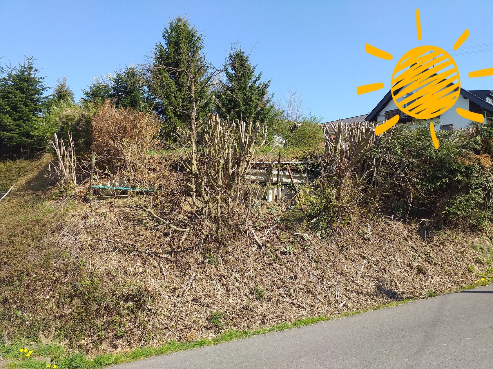 Hang mit trockenem Gebüsch, Gartenzaun, Haus im Hintergrund, orange Sonnezeichnung