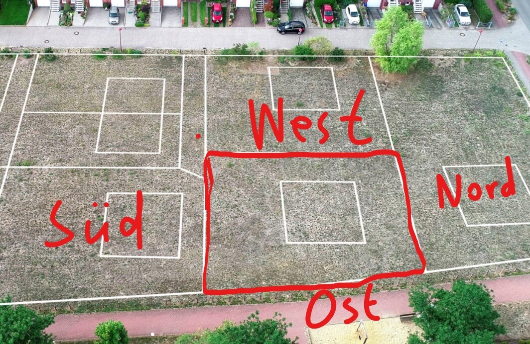 Luftaufnahme eines Sportfelds mit weißen Linien, rote Richtungsbeschriftung Süd, West, Nord, Ost.