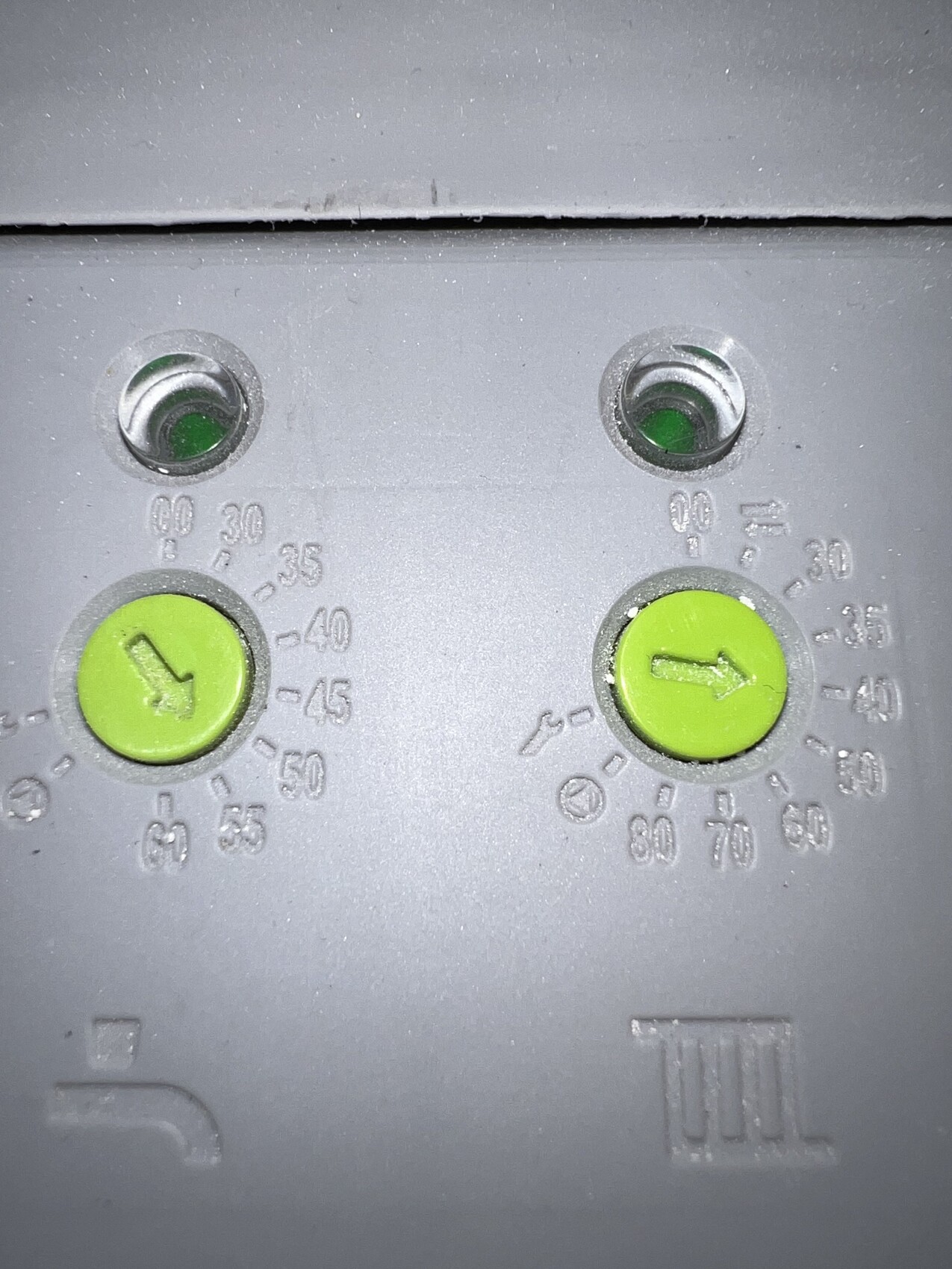 Zwei grüne Drehknöpfe mit Pfeilmarkierungen auf grauem Bedienfeld, Skala 0–90.