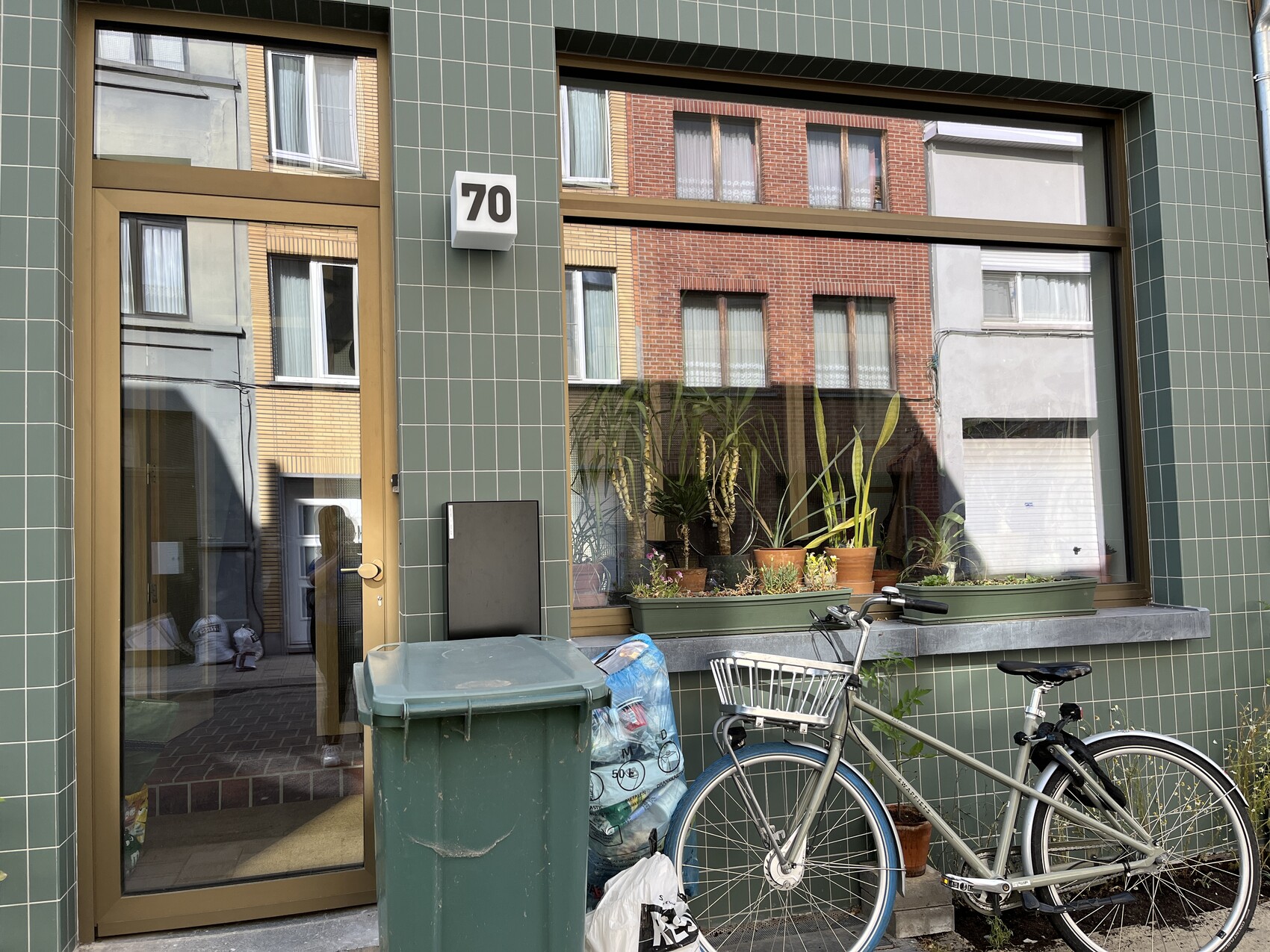 Grüne Kachelfassade mit Tür, Hausnummer 70, Fenster mit Pflanzen und Fahrrad davor
