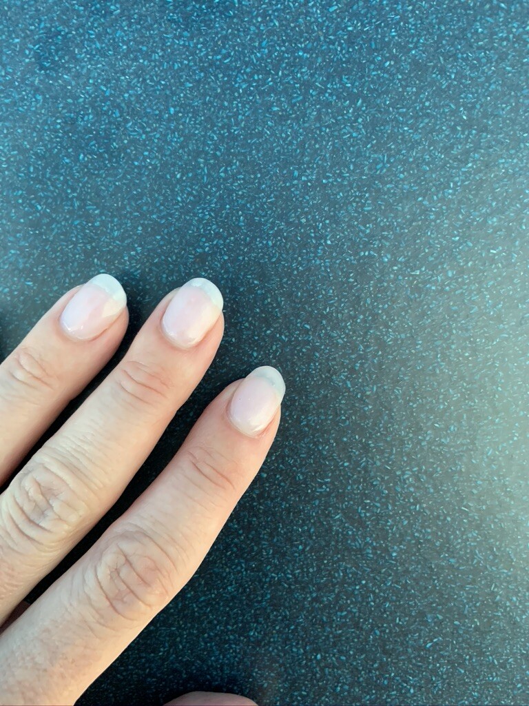 Nahaufnahme einer Hand mit kurzen, naturfarbenen Fingernägeln auf dunkler, strukturierter Oberfläche.