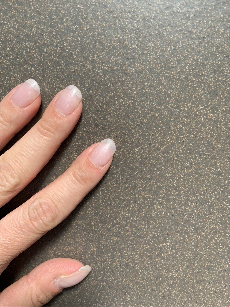 Nahaufnahme von drei Fingernägeln mit natürlichen, hellen Spitzen auf grauer Oberfläche.